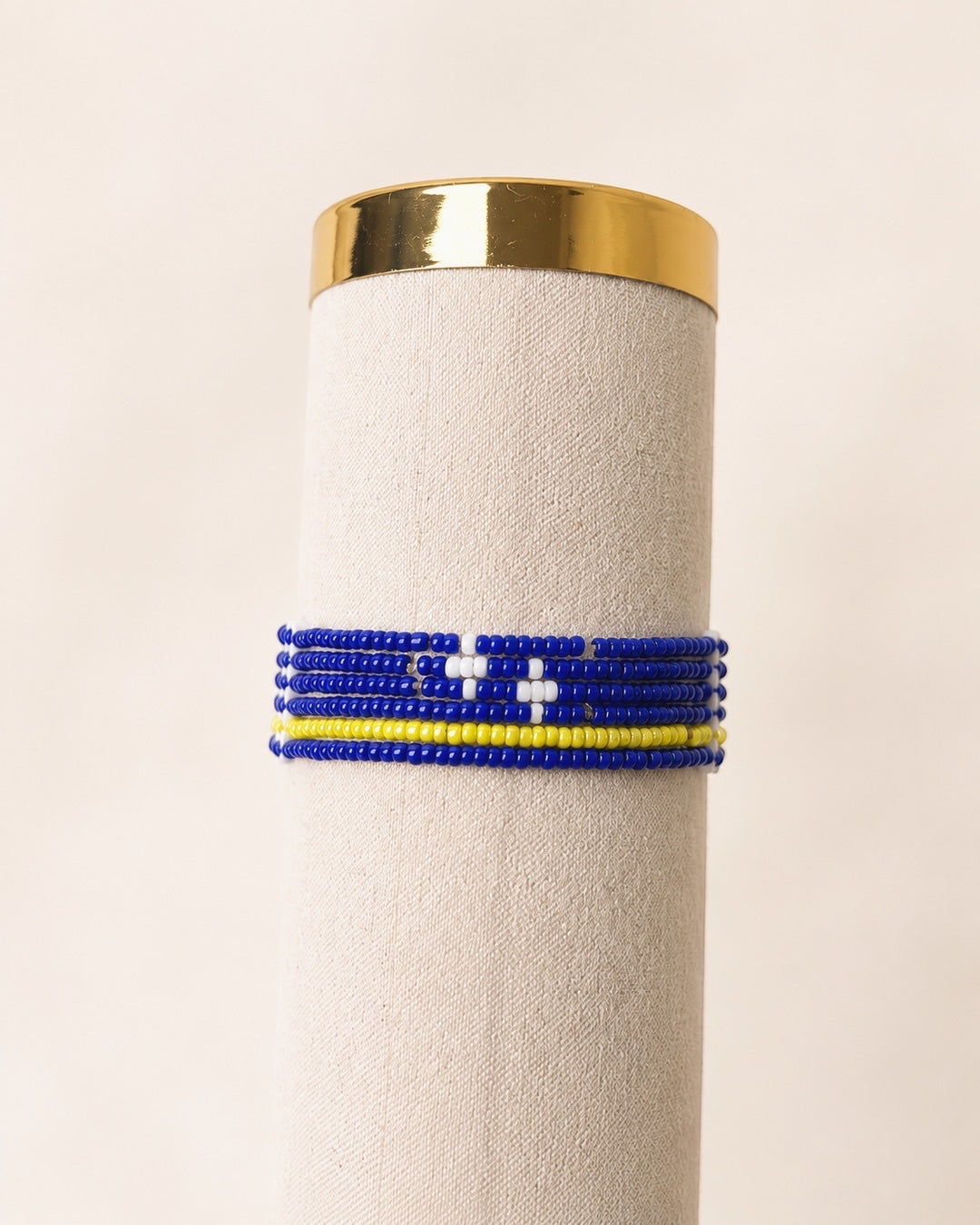 Handgemaakte Tintabeads Curaçao armband met blauwe, gele en witte kralen in zes verbonden rijen op een display.