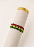 Tintabeads Ghana armband met rode, gele en groene kralen en een zwart sterdetail op een beige displayhouder.